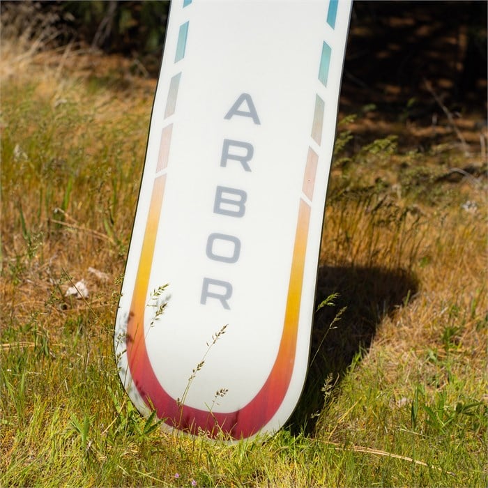 Arbor Women's Mantra Rocker Snowboard 2024 - A white snowboard with a red and yellow gradient stripe at the tip, featuring the word "ARBOR" in gray letters on its side.