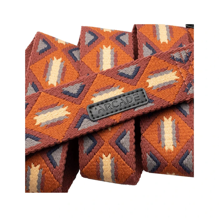 A close-up of a fabric belt with a geometric pattern in shades of orange, brown, grey, and beige. The belt is folded multiple times, displaying the texture and the word 'ARCADE' embossed on the surface.