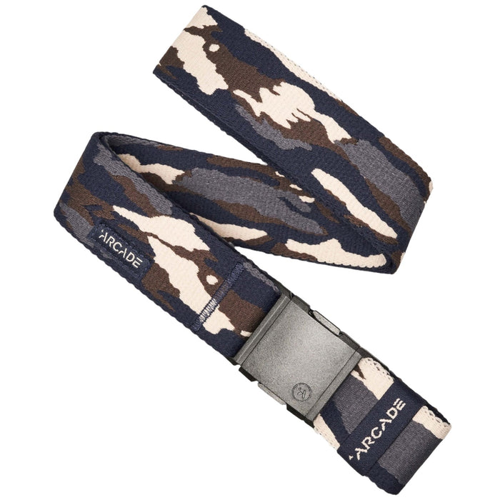 A camouflage-patterned belt in shades of blue, brown, and beige, laid flat with a black plastic buckle. The belt has a fabric tag with the word 'Arcade' stitched on it.