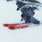 A person wearing a grey snow suit is skiing downhill on a pair of red and white Salomon S/Lab QST Blank skis.