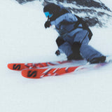 A person wearing a grey snow suit is skiing downhill on a pair of red and white Salomon S/Lab QST Blank skis.