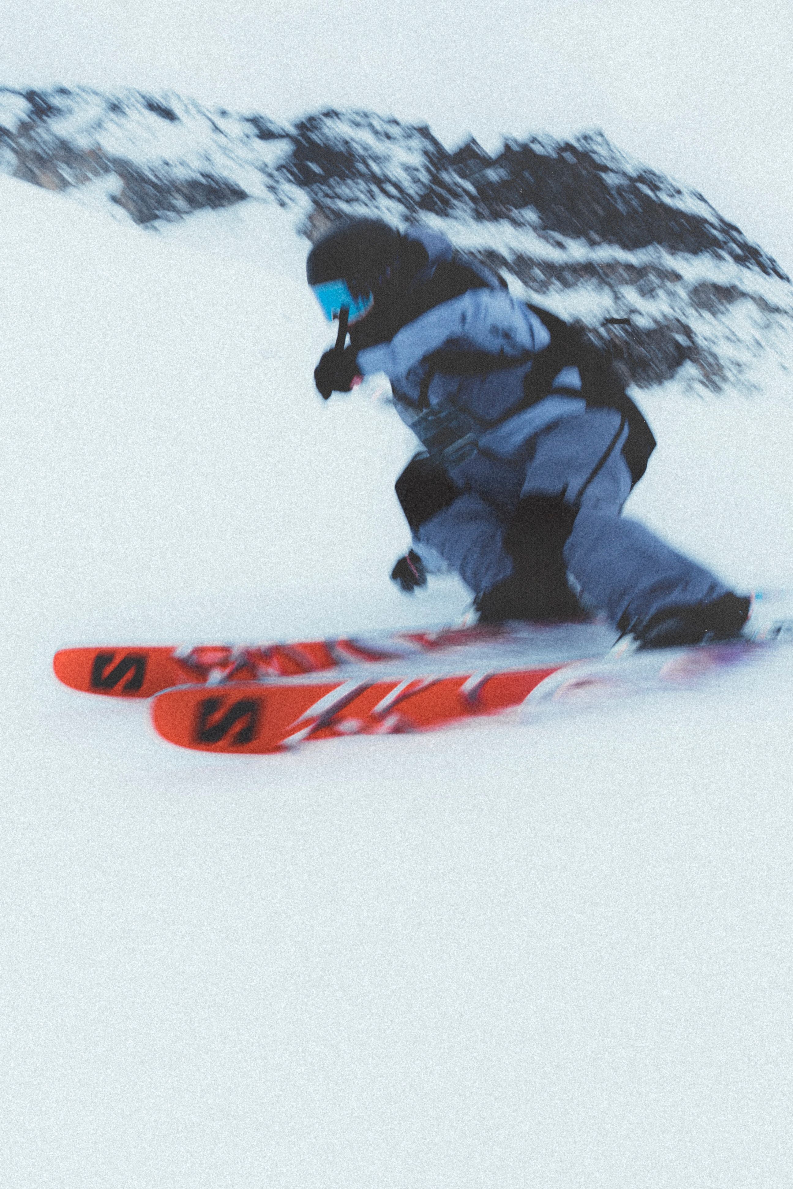 A person wearing a grey snow suit is skiing downhill on a pair of red and white Salomon S/Lab QST Blank skis.