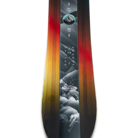 Junior twin-tip snowboard deck close-up with dark graphic and red-to-yellow gradient edge