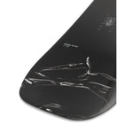 Ride Women's Magic Stick Snowboard 2025 - A black snowboard with a white logo and text on top, featuring a woman riding it in the background.
