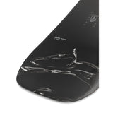 Ride Women's Magic Stick Snowboard 2025 - A black snowboard with a white logo and text on top, featuring a woman riding it in the background.