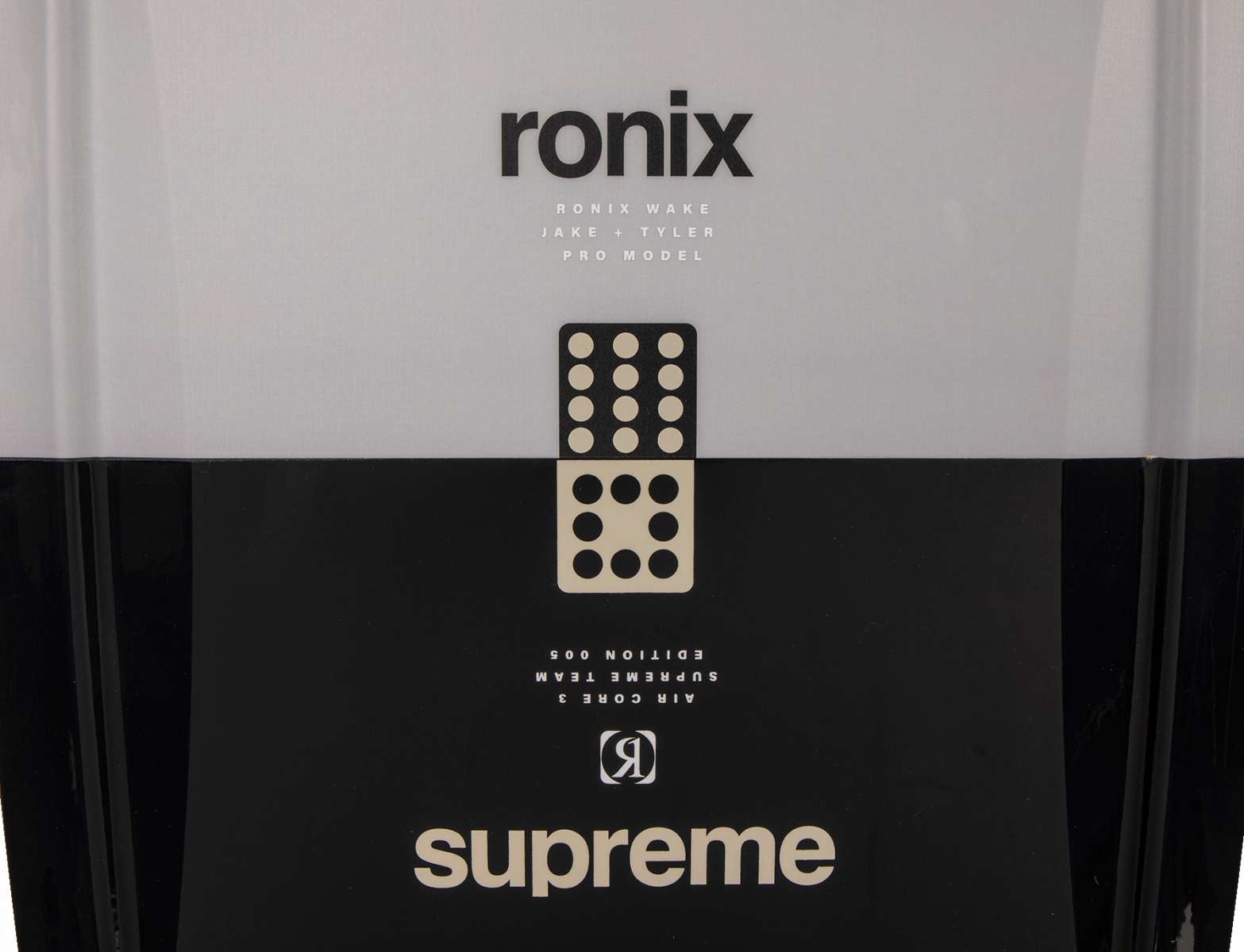 Ronix Supreme Wakeboard 2024 - A black wakeboard with a white logo and text on top, featuring a rider standing in front of it.