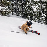 Völkl Peregrine 80 with Lowride 12 TCX Bindings - A skier in a tan and black snowsuit is skiing down a snowy slope, wearing the Völkl Peregrine 80 skis with Lowride 12 TCX bindings.