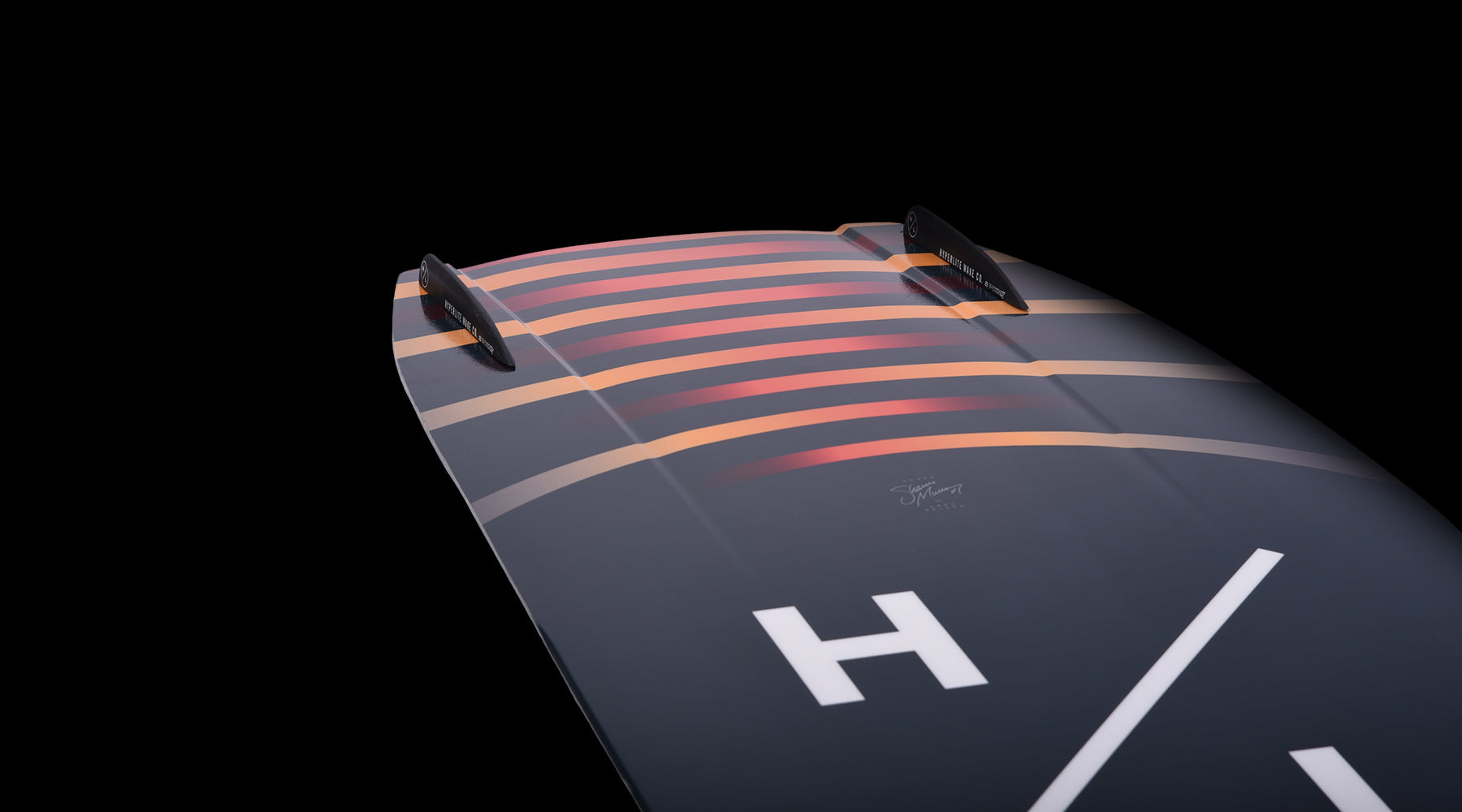 Hyperlite Baseline Wakeboard 2024 - A dark gray wakeboard with a white "H" logo on top and a red stripe along the bottom edge.