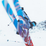 A person wearing a black jacket and skiing on snowy terrain. The skis are blue with red accents, and they have the brand name "Salomon S/Lab QST Blank Skis 2026" written on them.