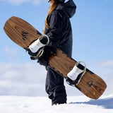 Jones Women's Flagship Snowboard 2024 - A brown snowboard with a black logo on top, held by a woman in a dark blue jacket and pants.