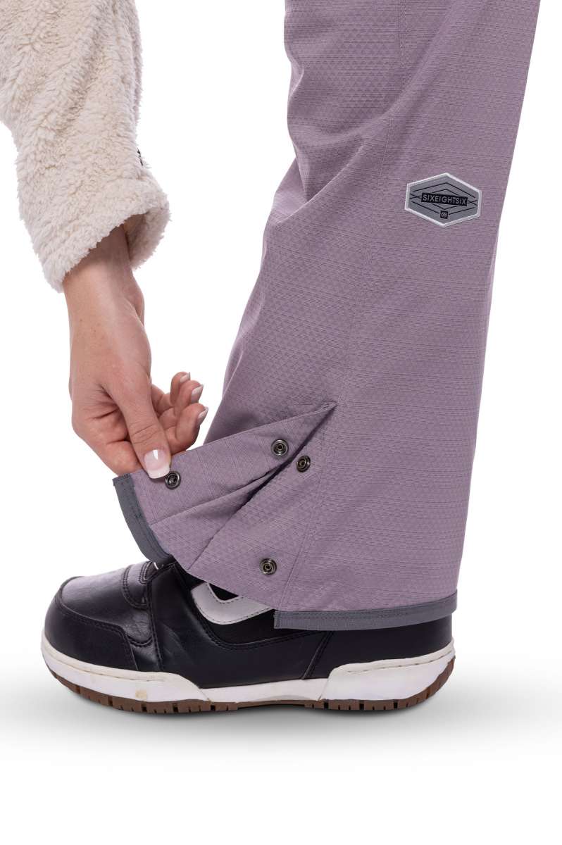 The 686 Black Magic insulated bib pants are primarily black with grey accents and have a zippered leg pocket on the right side.