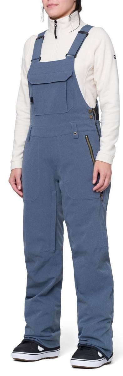 The 686 Women's Black Magic Insulated Bib 2024 is shown from the front view in black with zippered pockets and an adjustable waist strap.