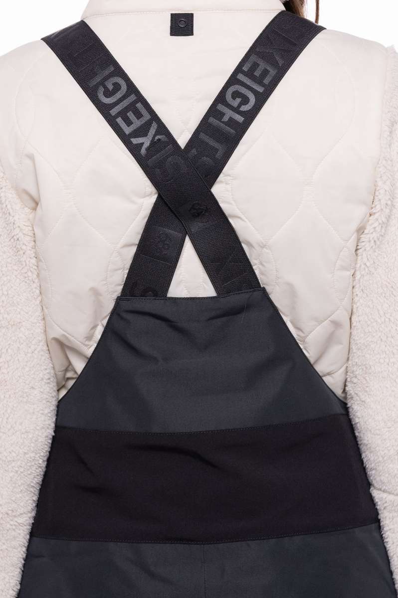 The 686 Women's Geode Thermagraph Bib 2023 is primarily black with a quilted pattern and a zippered leg closure.