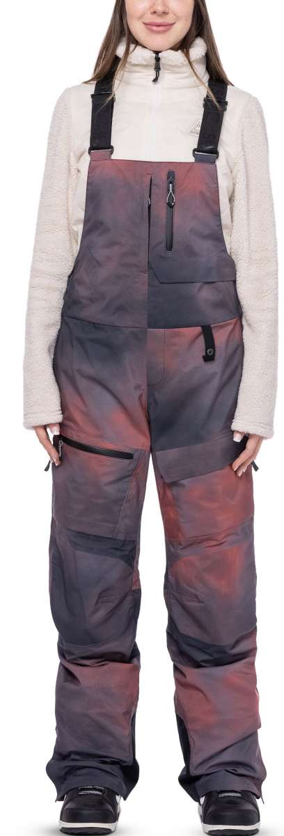 The 686 Women's Geode Thermagraph Bib 2023 features a black and pink color scheme with a large zipper pocket on the thigh.