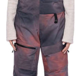 The 686 Women's Geode Thermagraph Bib 2023 features a black and pink color scheme with a large zipper pocket on the thigh.