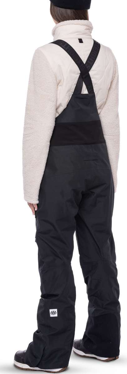 The 686 Women's Geode Thermagraph Bib 2023 is primarily black with an insulated hood and adjustable straps.