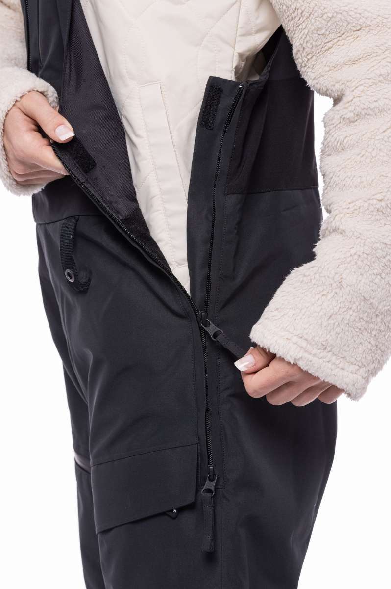 The 686 Women's Geode Thermagraph Bib 2023 is shown in black with an insulated hood and front zipper.