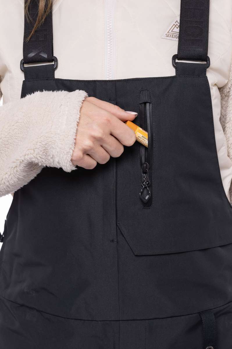 The 686 Women's Geode Thermagraph Bib 2023 is primarily black with an orange zipper and a black BOA dial.