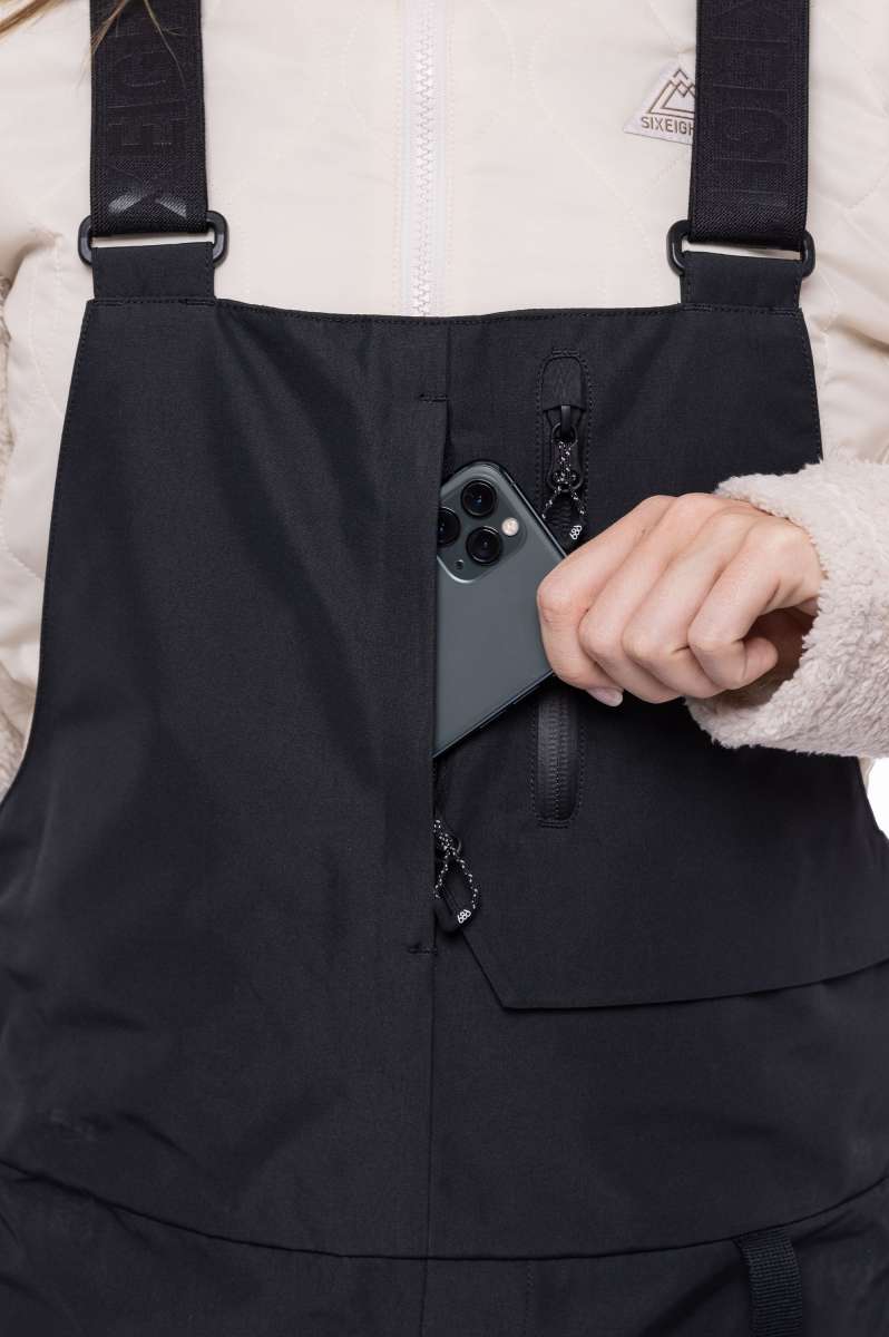 The 686 Women's Geode Thermagraph Bib has a solid black color with an insulated hood and is shown in a front view.