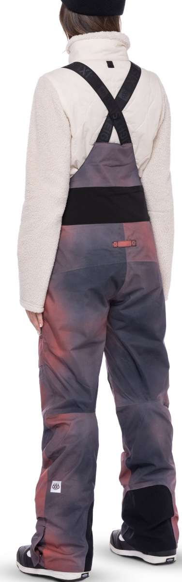 The 686 Women's Geode Thermagraph Bib 2023 has a purple and black color scheme with a distinctive geometric pattern on the front view.