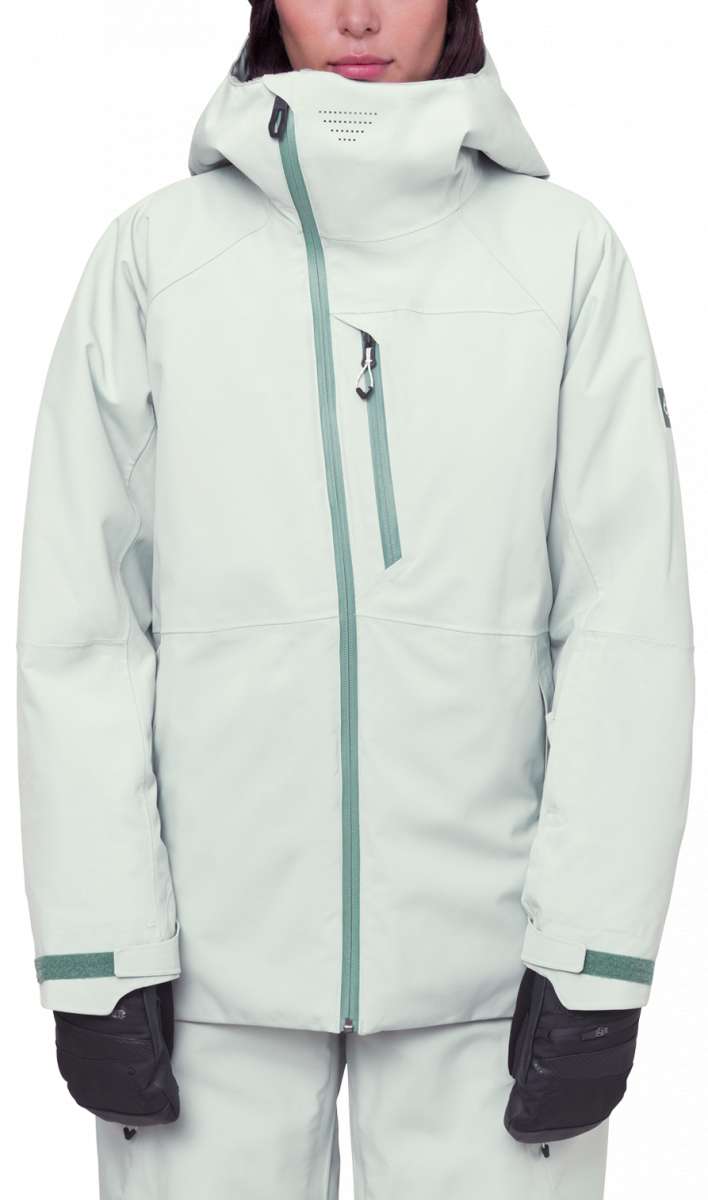The 686 Women's Hydra Insulated Jacket 2024 is primarily white with a green zipper and accents on the hood and cuffs.