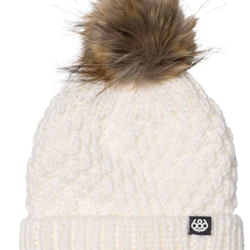 The 686 Majesty Beanie has a white cable knit design with a brown faux fur pom-pom on top.