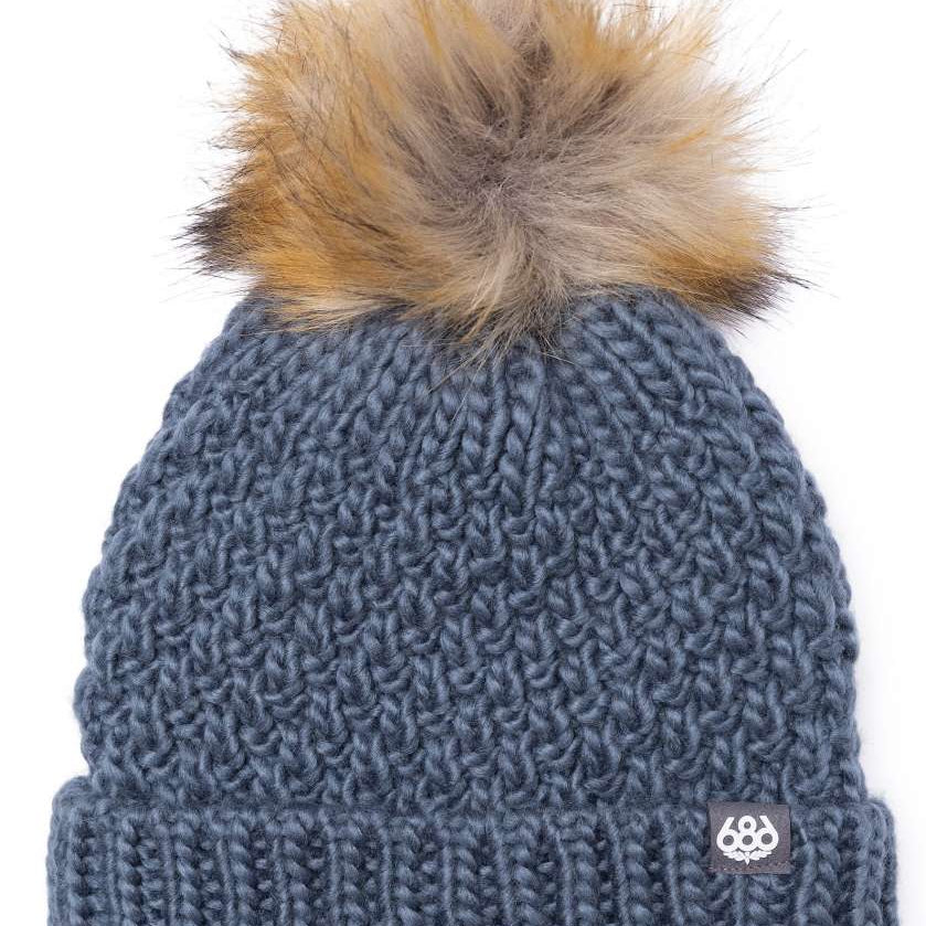 The 686 Majesty beanie is dark gray with a tan faux fur pom-pom on top.