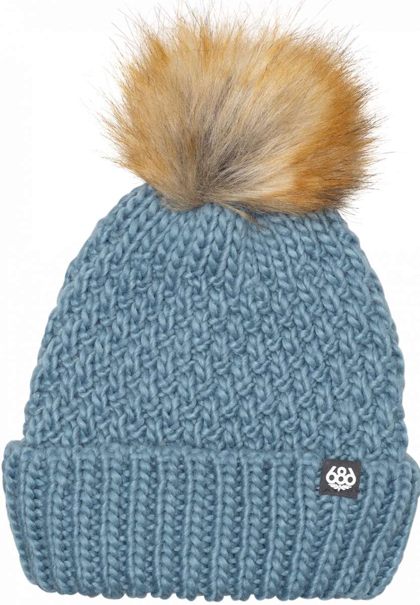 The 686 Ladies Majesty Cable Knit Beanie 2024 is light blue with a ribbed cuff and a large brown faux fur pom-pom on top.
