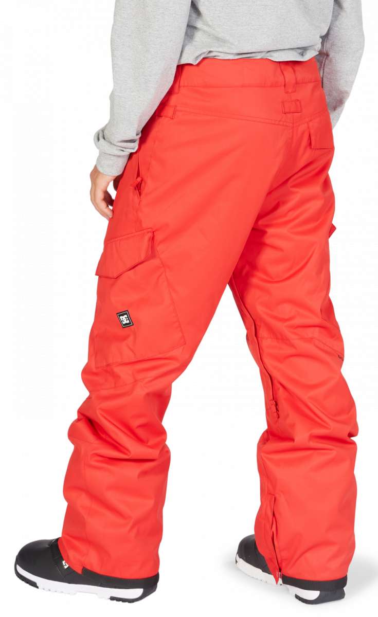 DC Banshee Insulated Pant 2023 - A pair of bright red snow pants with cargo pockets on the side and a black logo patch near the bottom left leg.