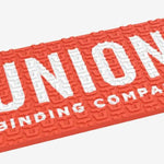 Union Surf Stomp Pad - A coral-colored pad with a textured surface, featuring a repeating pattern of stylized "U" letters in white.