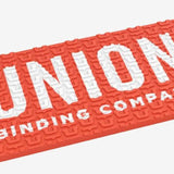 Union Surf Stomp Pad - A coral-colored pad with a textured surface, featuring a repeating pattern of stylized "U" letters in white.