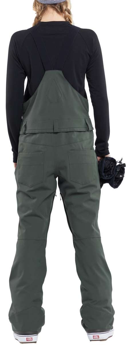 Volcom Women's Swift Bib Overall Pant 2024 - Dark green bib overalls with a black top and white soles on the feet in the image.