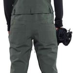 Volcom Women's Swift Bib Overall Pant 2024 - Dark green bib overalls with a black top and white soles on the feet in the image.