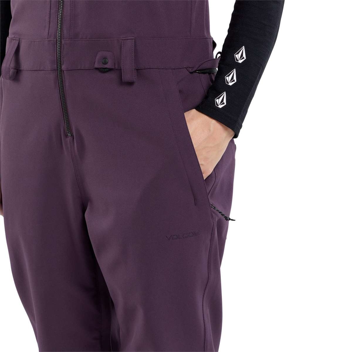 Volcom Women's Swift Bib Overall Pant 2024 - A pair of purple snow pants with a black zipper on the left side and a small logo that says "VOLCOM" in black letters near the bottom right leg.