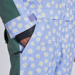 Airblaster Women's Freedom Insulated Suit 2024 - A light blue snowsuit with a repeating pattern of white flowers and yellow centers, featuring a green sleeve on the left side.