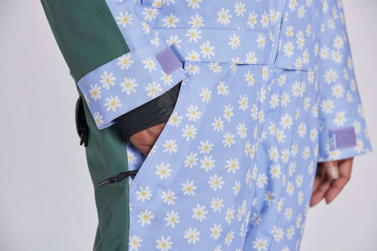 Airblaster Women's Freedom Insulated Suit 2024 - A light blue snowsuit with a repeating pattern of white flowers and yellow centers, featuring a green sleeve on the left side.