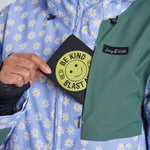 Airblaster Women's Freedom Insulated Suit 2024 - A woman wearing a light blue snowsuit with white daisies and yellow centers, holding it up to show off the front zipper and black logo on the chest.