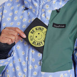 Airblaster Women's Freedom Insulated Suit 2024 - A woman wearing a light blue snowsuit with white daisies and yellow centers, holding it up to show off the front zipper and black logo on the chest.