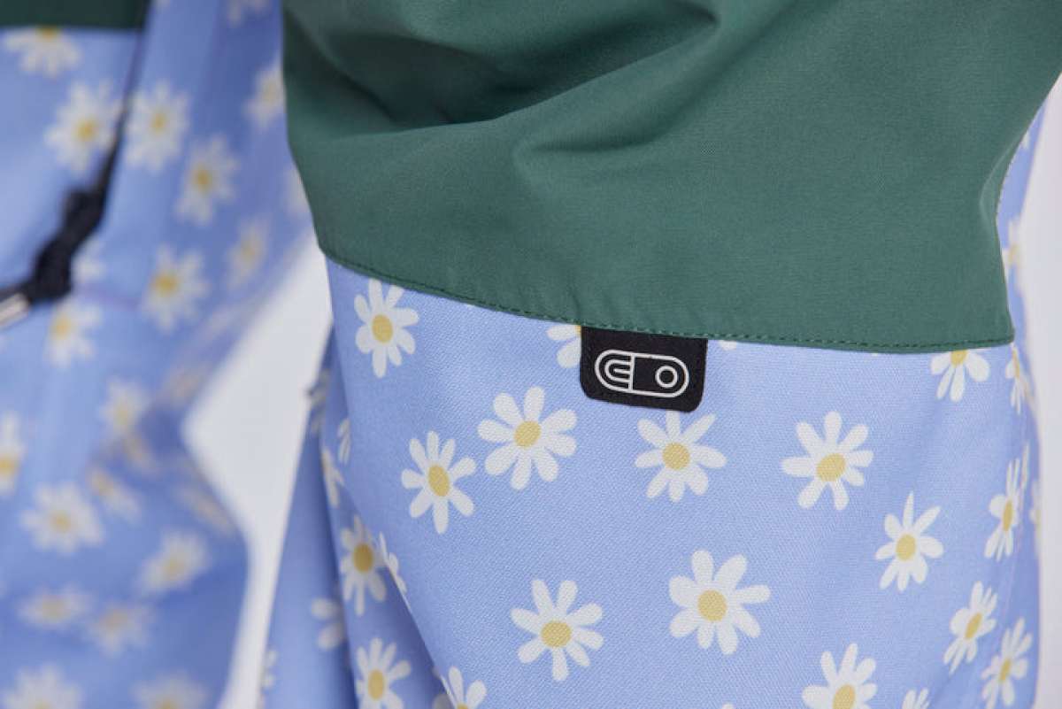 Airblaster Women's Freedom Insulated Suit 2024 - A light blue snowsuit with a repeating pattern of white flowers and yellow centers, featuring a black tag with "EO" in white text on the waistband.