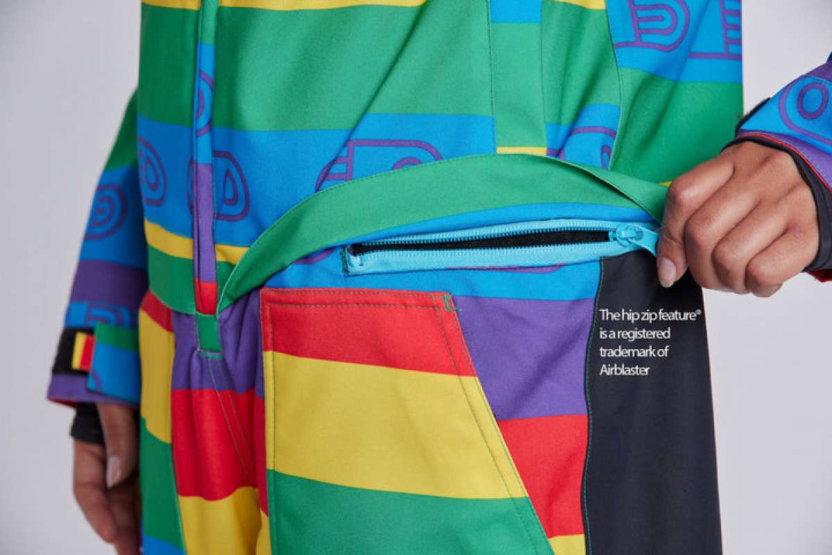 Airblaster Women's Freedom Stretch Suit 2024 - A woman wearing a multicolored, rainbow-striped snowsuit with purple accents and a black strap across her chest.