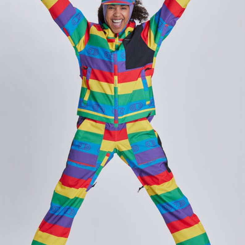 Airblaster Women's Freedom Stretch Suit 2024 - A woman wearing a rainbow-striped, multicolored snowsuit with black accents and a matching hat.