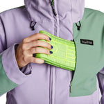 Airblaster Women's Stretch Freedom Suit 2023 - Woman wearing a purple and green snowsuit with a hood, holding a neon yellow wallet in her hand.