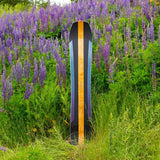Arbor Annex Bi-Camber Snowboard 2023 - A black snowboard with a yellow stripe down the middle, standing in front of a field of purple flowers and green grass.
