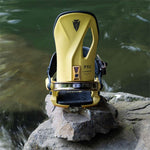 Arbor Cypress Snowboard Bindings 2024 - A pair of yellow snowboard bindings with black straps and buckles, sitting on a rock near water.