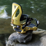 Arbor Cypress Snowboard Bindings 2024 - A pair of yellow snowboard bindings with black straps and buckles, sitting on a rock near a body of water.