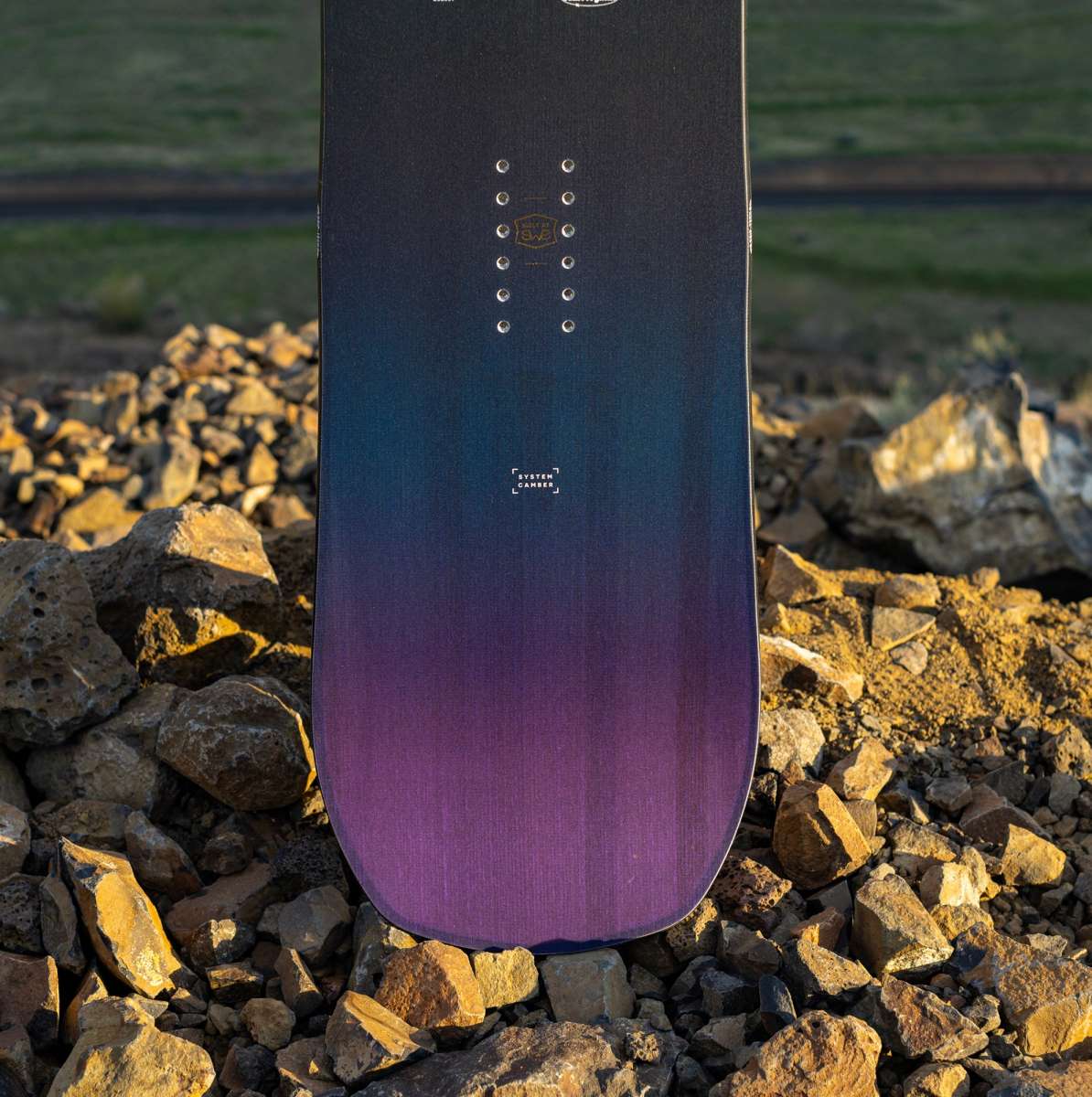 Arbor Draft Camber Snowboard 2024 - A black snowboard with a subtle white logo and silver screws on top of a rocky surface.