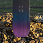 Arbor Draft Camber Snowboard 2024 - A black snowboard with a subtle white logo and silver screws on top of a rocky surface.