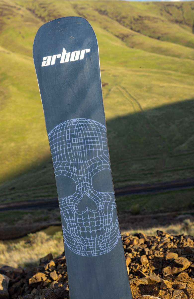 Arbor Draft Camber Snowboard 2024 - A black snowboard with a white geometric pattern on top of a rocky hillside.