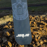 Arbor Draft Camber Snowboard 2024 - A black snowboard with a white spiderweb design on top of a pile of rocks.