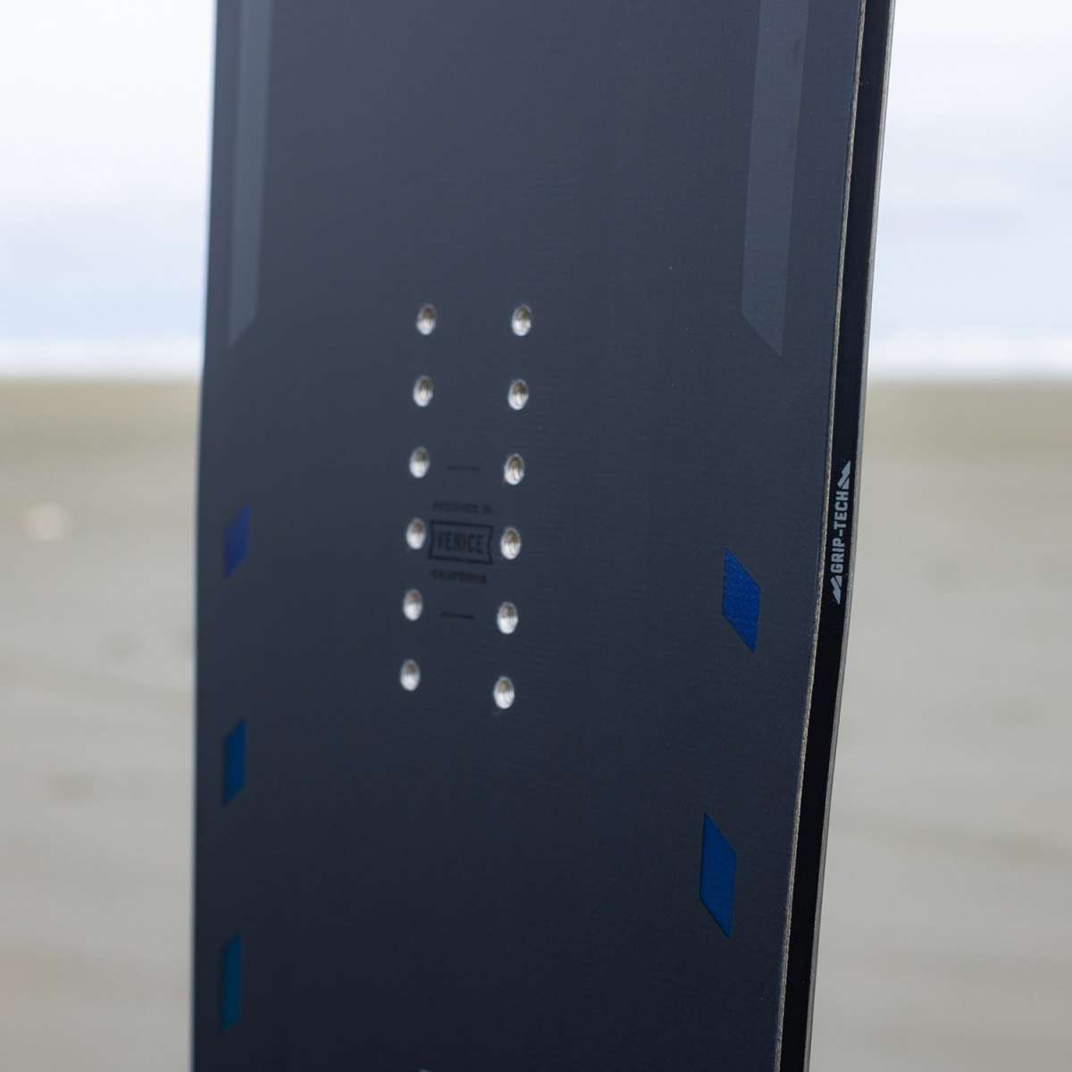 Arbor Formula Rocker Snowboard 2024 - A dark gray snowboard with a geometric pattern of lighter gray lines and shapes on top, featuring blue accents along the edges.